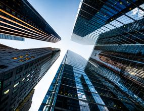 Perspectiva vertical entre edifícios corporativos contemporâneos, destacando arquitetura, escala e convergência de estruturas. A composição remete à visão estratégica, governança, solidez institucional e integração necessárias para estruturar a inovação n