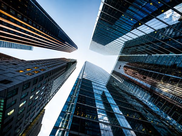Perspectiva vertical entre edifícios corporativos contemporâneos, destacando arquitetura, escala e convergência de estruturas. A composição remete à visão estratégica, governança, solidez institucional e integração necessárias para estruturar a inovação n